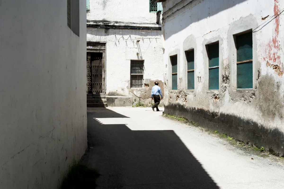 Un passant traverse une ruelle de Stone Town entre façades blanches et volets verts.