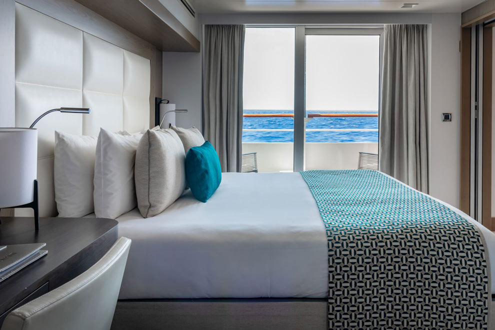 Une cabine de bateau Ponant avec lit double et balcon offrant une vue sur la mer.