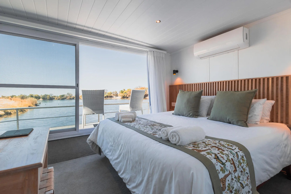Une cabine lumineuse du Chobe Princess avec lit double et balcon offrant une vue sur une rivière paisible.
