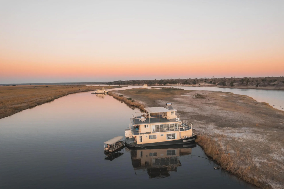 Un bateau navigue sur la rivière Chobe au coucher du soleil dans un paysage sauvage.