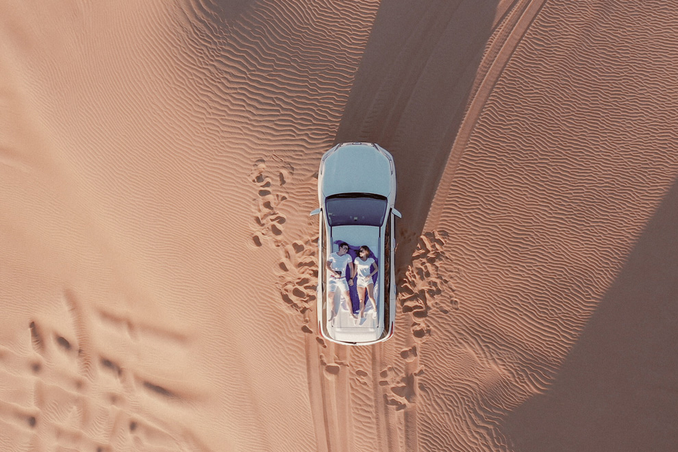 Vue aérienne d’un couple allongé dans une voiture au milieu des dunes de Namibie.