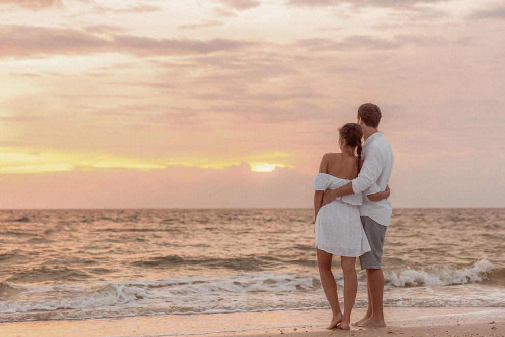 Couple enlacé regardant le coucher de soleil face à la mer aux Seychelles.