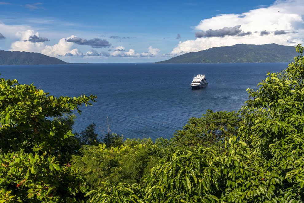Un bateau navigue sur une mer calme entre des îles verdoyantes sous un ciel partiellement nuageux.