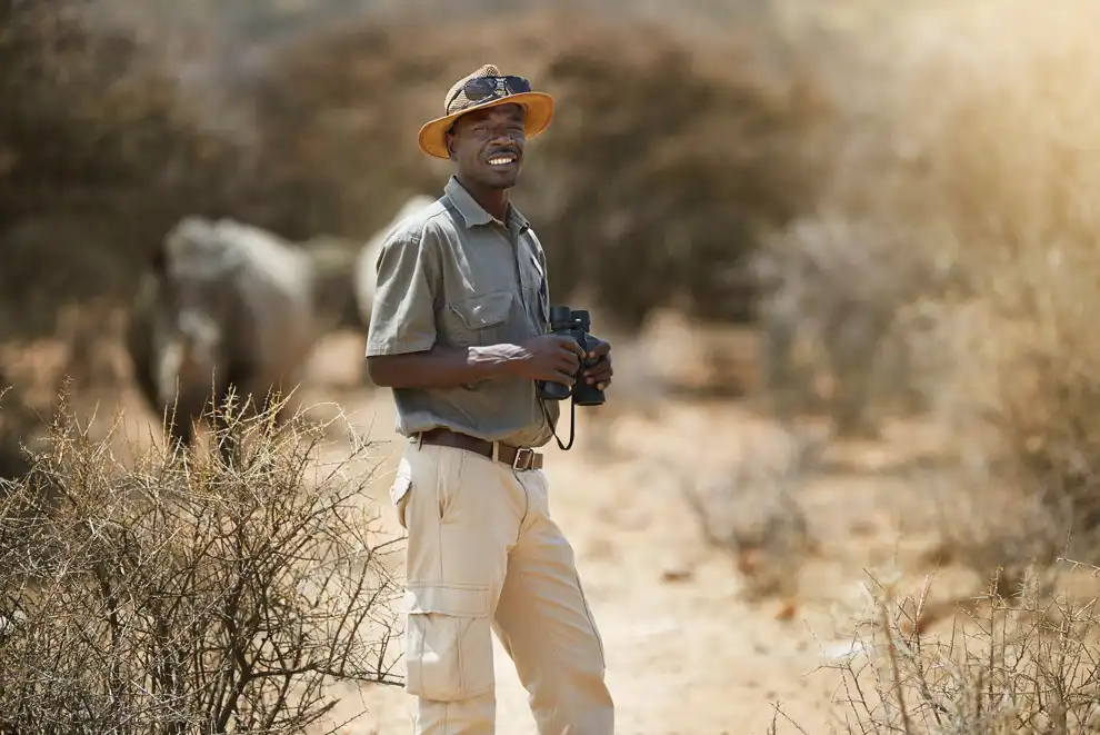 Guide de safari souriant avec des jumelles, en brousse africaine.