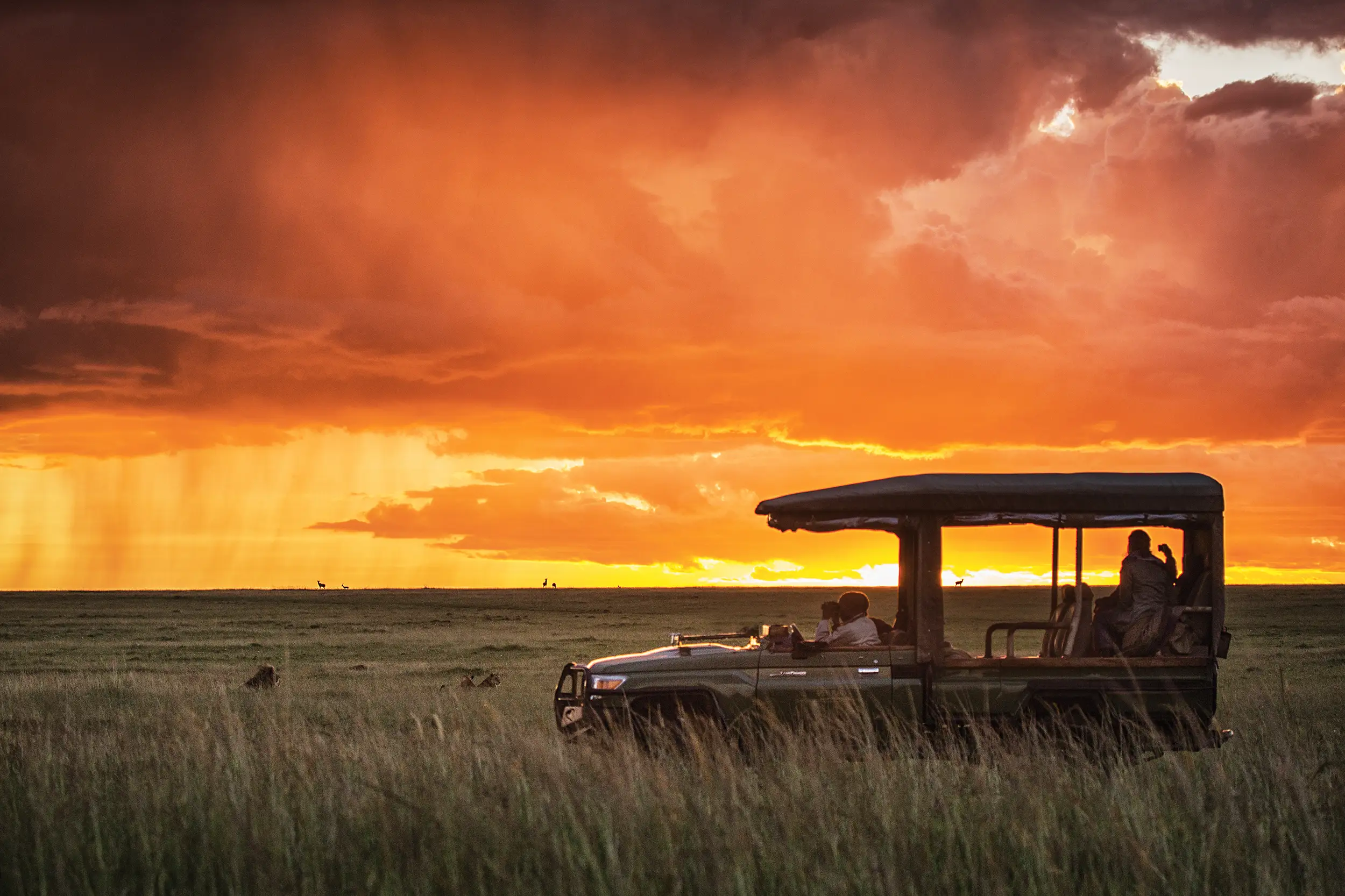 Voyage au Kenya : véhicule de safari dans la savane du Masaï Mara au coucher du soleil, avec un ciel orangé spectaculaire.