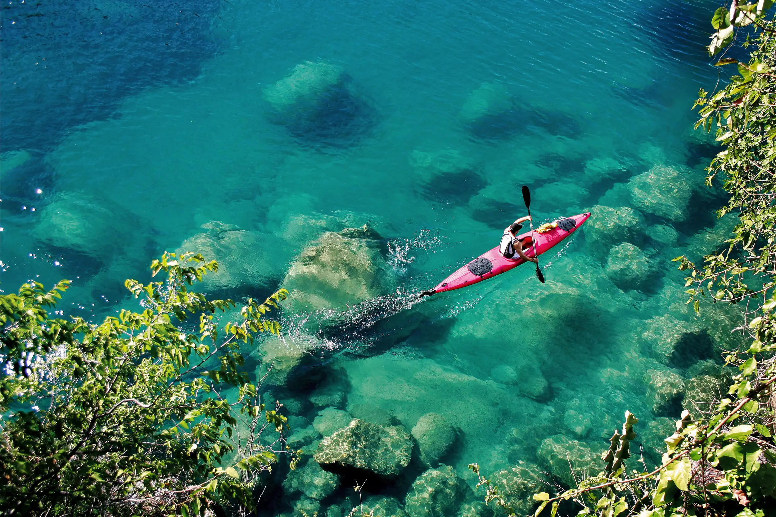 Voyage au Malawi : un kayak glisse sur les eaux turquoise du lac Malawi, entouré de roches et de végétation tropicale.