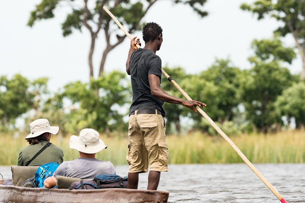 Pirogue guidée par un local sur une rivière, avec deux voyageurs observant la nature environnante.