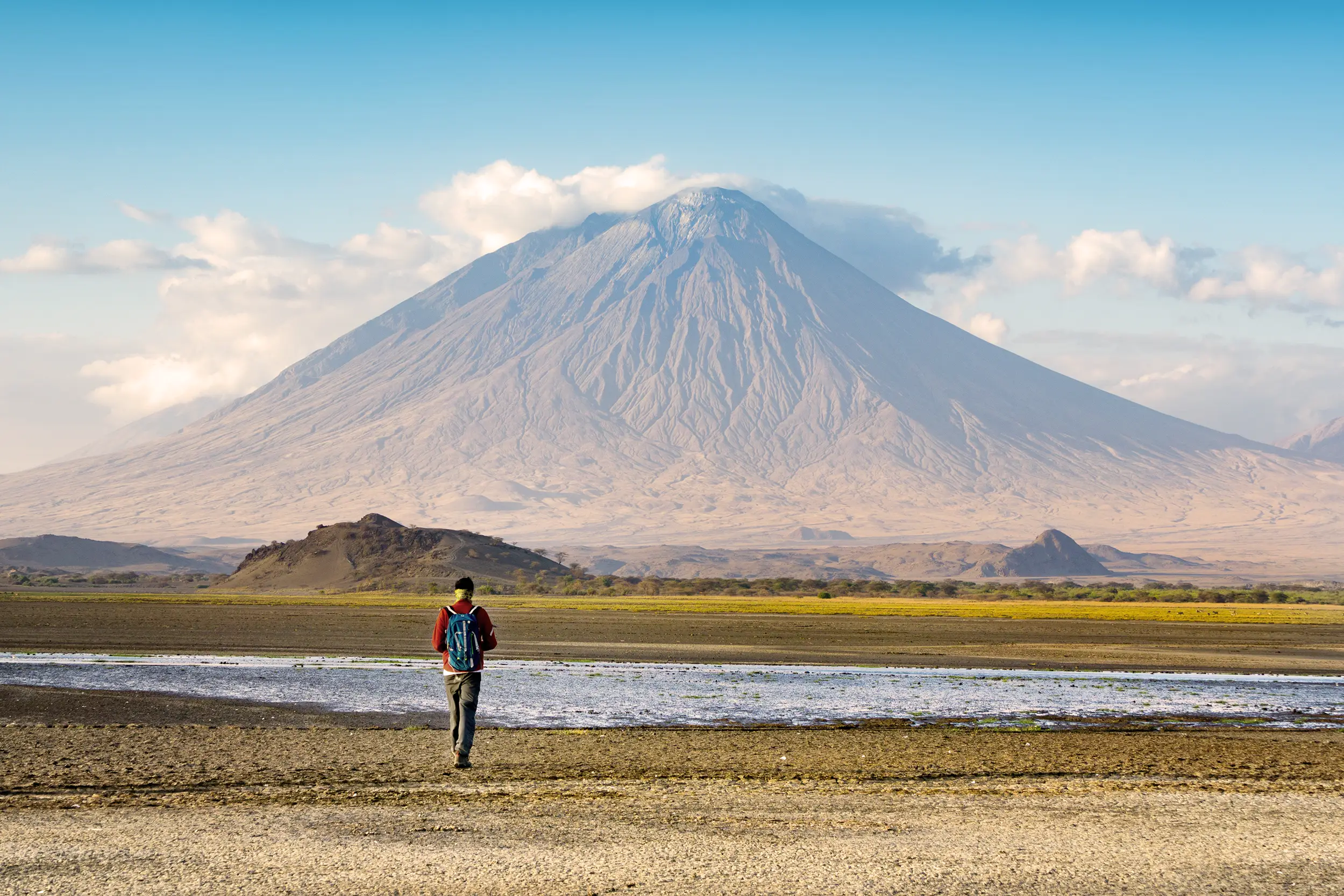 Voyageur marchant vers la montagne Ol Doinyo Lengai au lac Natron, symbole de départ pour un voyage en Afrique avec Mungo Park.