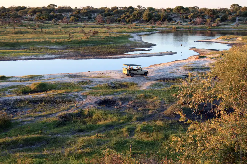 Véhicule de safari au bord d’une rivière au coucher du soleil, symbole de l’expertise terrain de Mungo Park en Afrique.