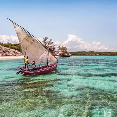 Un boutre traditionnel naviguant sur les eaux turquoise au large de Madagascar, sous un ciel tropical clair.