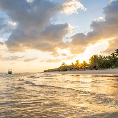 Lumière dorée d’un coucher de soleil sur la plage du Mozambique, avec un bateau au large et des palmiers le long du rivage – scène paisible évoquant la douceur de voyager en Afrique australe.