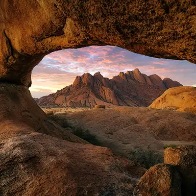 Paysage du Spitzkoppe en Namibie, où les roches rouges encadrent un coucher de soleil sur les montagnes du désert du Namib.