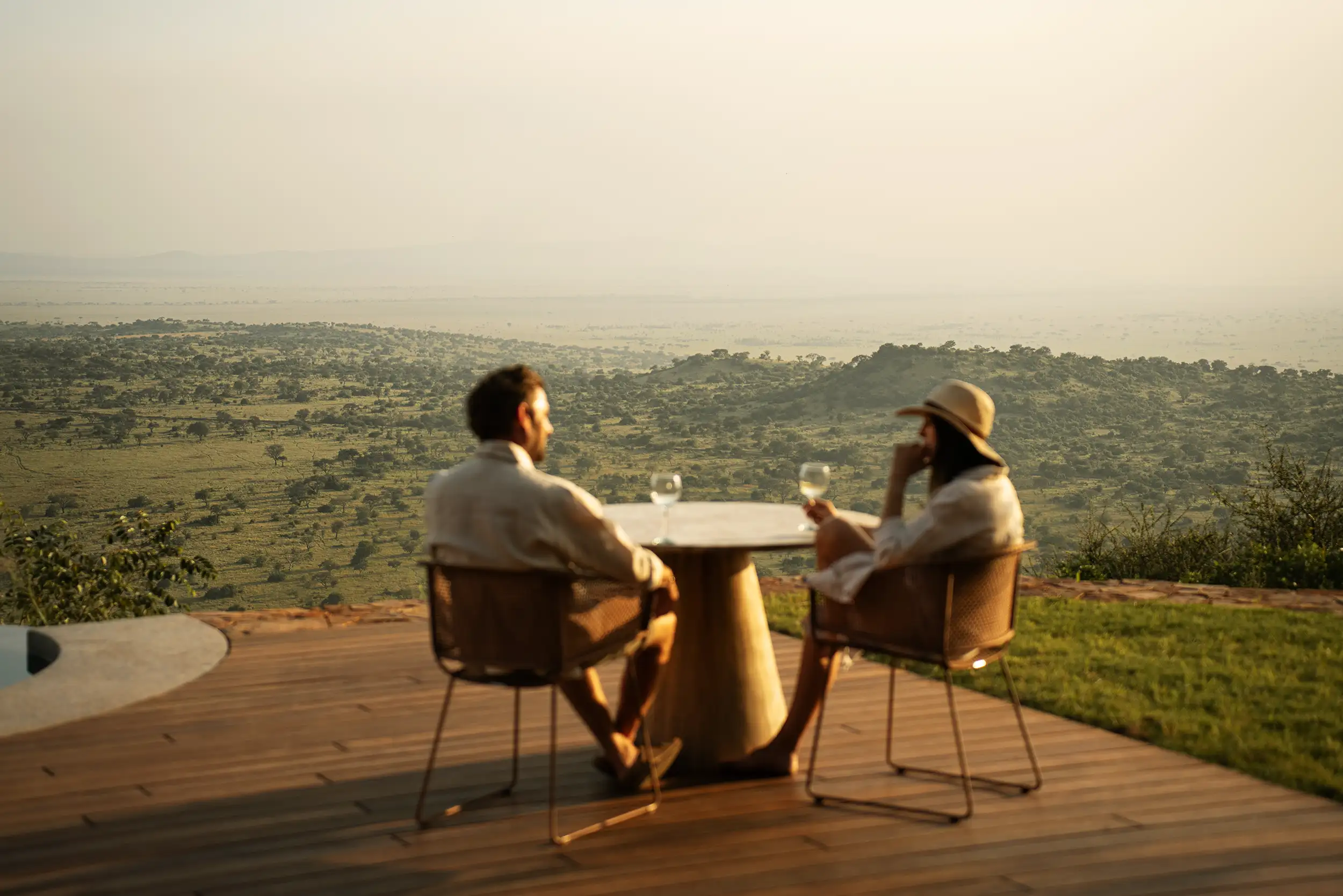 Deux voyageurs partagent un moment calme autour d’une table, face à la savane africaine au coucher du soleil.