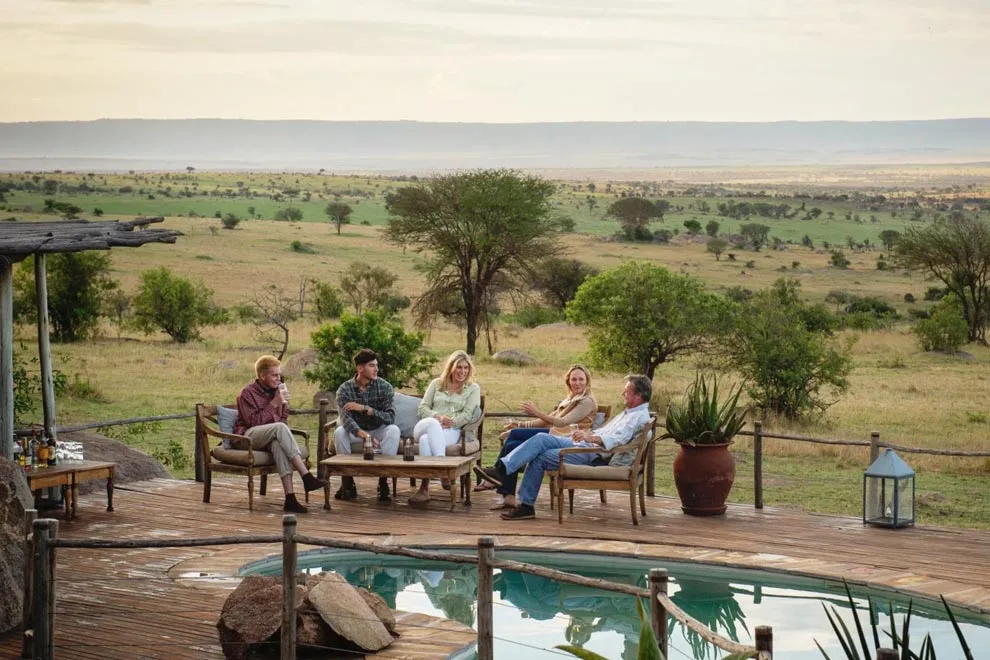 Un groupe de personnes se détend sur une terrasse avec vue sur la savane près d’une petite piscine en Tanzanie.