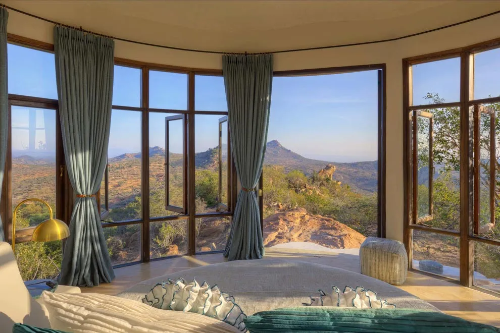 Une chambre lumineuse avec grandes baies vitrées offrant une vue panoramique sur un paysage montagneux.