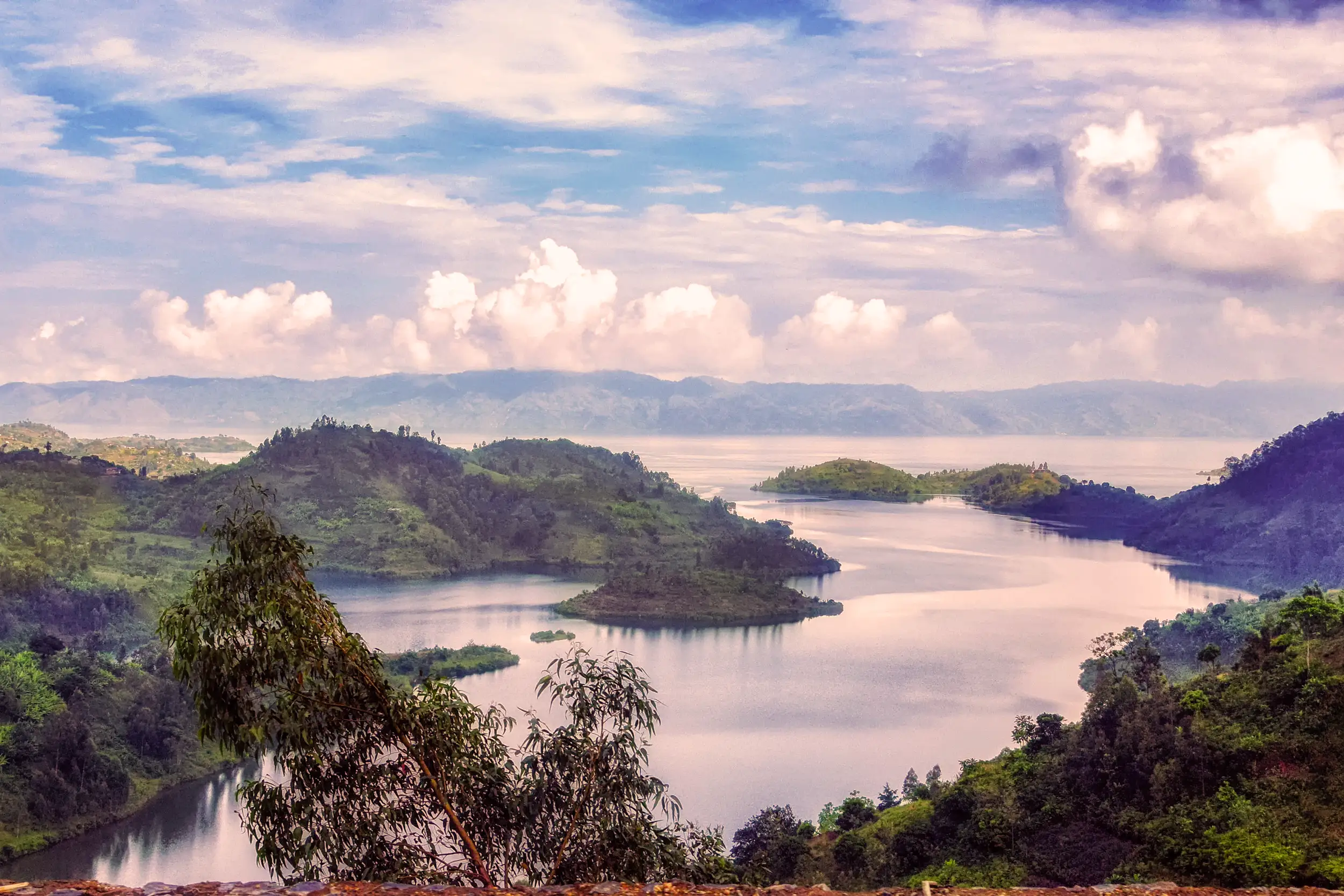 Voyage au Rwanda : vue panoramique sur un lac entouré de collines verdoyantes et de nuages, symbole de la beauté naturelle des Grands Lacs d’Afrique.
