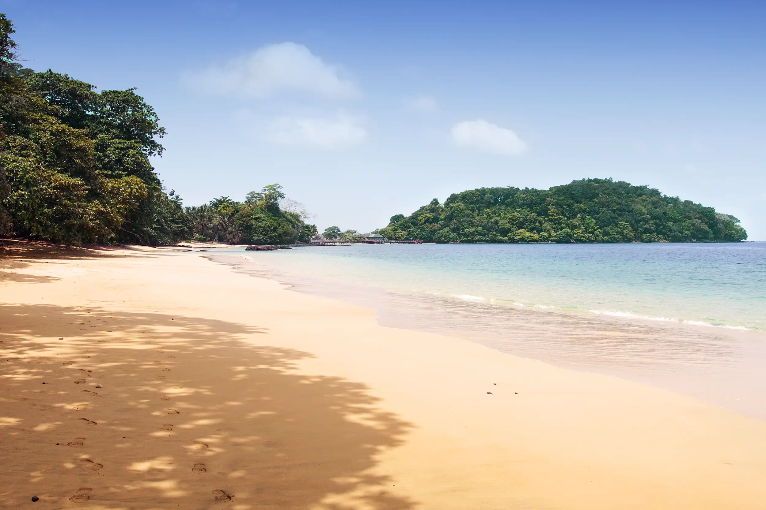 Voyage à São Tomé : plage de sable doré bordée de forêt tropicale et d’eaux turquoise dans le golfe de Guinée.