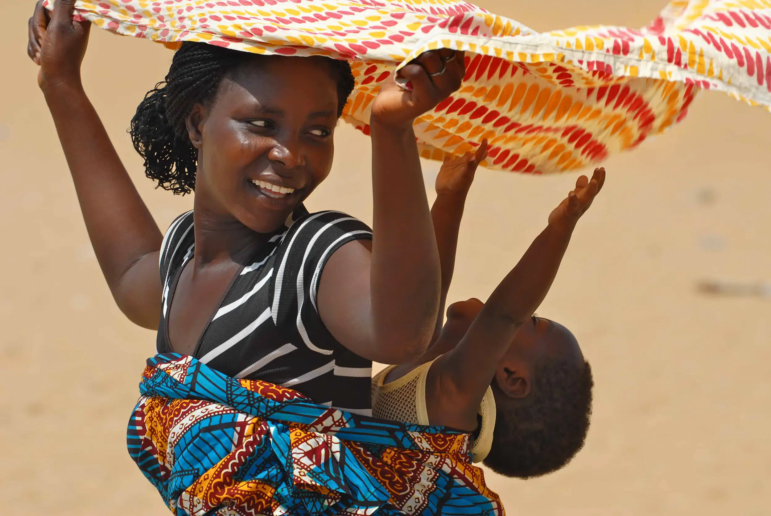 Voyage en Afrique de l’Ouest : femme souriante portant son enfant dans un pagne coloré, symbole de la chaleur et des traditions africaines.