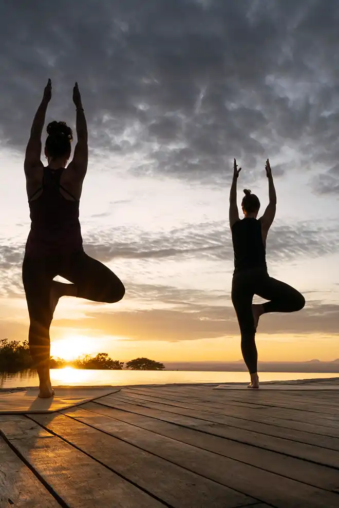 Deux voyageuses pratiquant le yoga en plein air, face à la savane africaine.