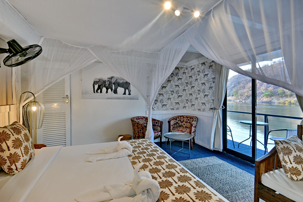 Cabine élégante du Zambezi avec lit à baldaquin et moustiquaire, décorée sur le thème de la faune, avec vue sur une rivière.